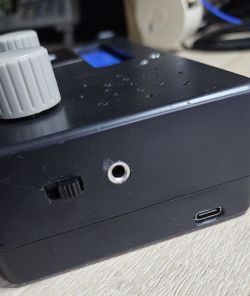 Zbliżenie na czarną obudowę urządzenia elektronicznego z gniazdem mini-jack, przełącznikiem, portem USB-C i dwoma pokrętłami.