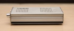 Side view of a silver headphone amplifier on a wooden surface.