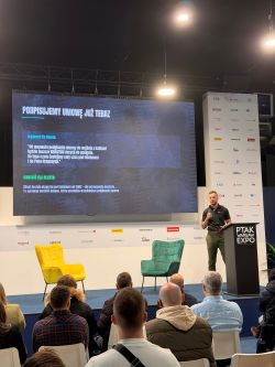 Talk on a PTAK Warsaw Expo stage; man at a lectern and a slide reading “Podpisujemy umowę już teraz”
