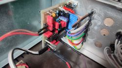 Zbliżenie na wnętrze obudowy urządzenia elektronicznego z widoczną płytką drukowaną, przewodami i radiatorami.