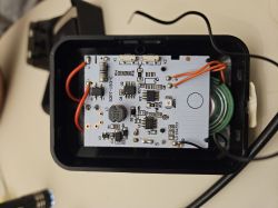 Wnętrze uszkodzonego dzwonka bezprzewodowego z widoczną płytką drukowaną i odłączonym przewodem.