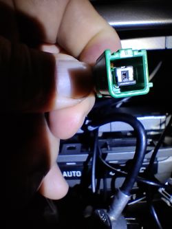 Zielone złącze car audio trzymane w dłoni, z widocznym wnętrzem złączki, w słabo oświetlonym otoczeniu.