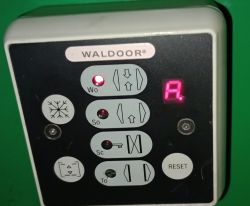 Panel kontroli drzwi z wyświetlaczem pokazującym literkę A i przyciskiem Reset.