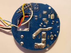 Round blue PCB underside with soldered wires and large metal traces, close-up