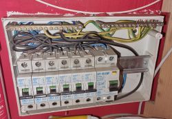 Panel elektryczny z licznymi bezpiecznikami i przewodami, bez osłony, z widocznym kurzem.