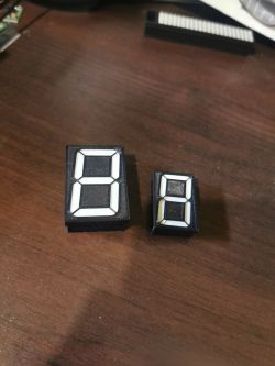 Two black seven-segment digit modules with white segments on a wooden tabletop