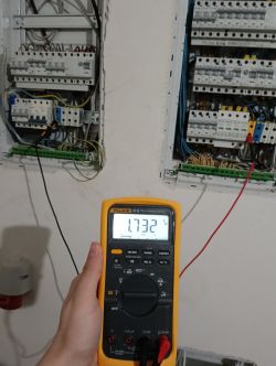 Miernik pokazujący napięcie 17.32 V przed dwoma rozdzielnicami elektrycznymi.