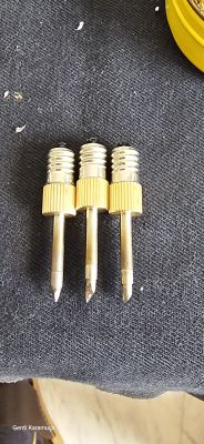 Three interchangeable tool bits with metallic threads and golden handles lying on dark fabric.