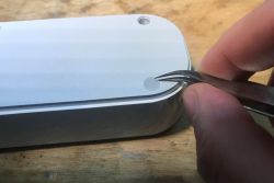 Tweezers lift a rubber foot on the underside of a white Gembird power strip.