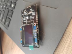 ESP8266 module with attached OLED display lying on a laptop.