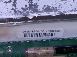 Zbliżenie na wewnętrzny komponent elektroniczny z widocznym uszkodzeniem i naklejką z kodem kreskowym.