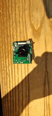 Green PCB with a camera lens on a wooden tabletop in strong light