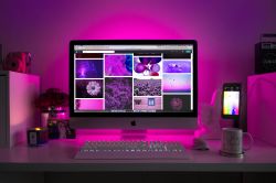 Desk with Computer and Pink Lighting A computer on a desk with pink lighting, displaying a collection of images in purple tones.