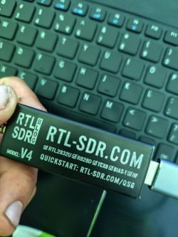 Tuner RTL-SDR V4 trzymany nad klawiaturą laptopa