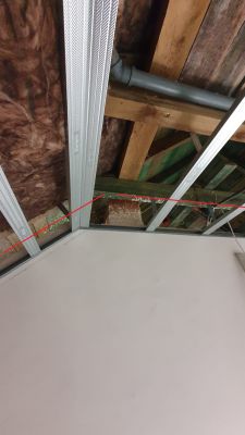 Widok od spodu na sufit z metalowymi profilami i rurą w systemie wentylacyjnym.