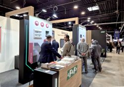 F&amp;F trade fair booth with a counter and brochures; visitors talk in an exhibition hall.