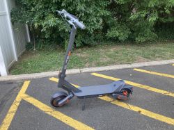 Elektryczna hulajnoga Yadea ElitePrime zaparkowana na asfalcie, otoczona zielenią.