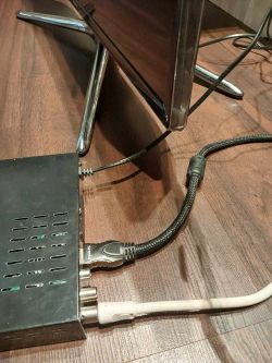 Dekoder podłączony do telewizora za pomocą kabli na drewnianej podłodze.