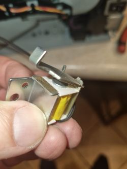 Zbliżenie na metalowy elektromagnes z dźwignią i filcem, trzymany w palcach.