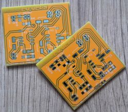Two yellow printed circuit boards with visible traces and markings on a wooden background.