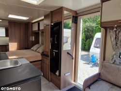 Interior of a modern camper with a kitchen, bed, and open door to the outside.