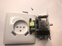 Disassembled in-wall socket: white faceplate, module and PCB with transformer, plus loose screws on a table