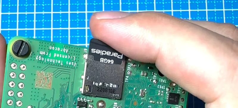 Dłoń wkładająca kartę pamięci microSD do płytki drukowanej Raspberry Pi.
