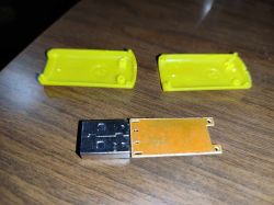 Rozebrane urządzenie USB z pustą płytką PCB i żółtą plastikową obudową na drewnianym stole