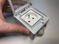 Close-up of a hand opening the lid of an outdoor French-type electrical socket.