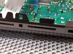 Zbliżenie na zieloną płytkę drukowaną z elementami elektronicznymi i taśmą przewodzącą.