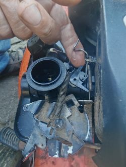 Zbliżenie mechanizmu przepustnicy kosiarki z widocznymi sprężynami i linką.