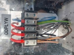 Wnętrze rozdzielni elektrycznej z wyraźnie widocznymi przewodami w różnych kolorach, w tym niebieskim, czerwonym, zielono-żółtym i brązowym.
