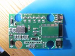 Circuit board with visible electronic components such as resistors, capacitors, and a PH9SFF25K6D chip on a wooden background.