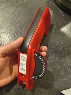 Red handheld Dymo label embosser with black rotary character wheel