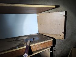 Cabinet with damaged doors and a hammer on the shelf.