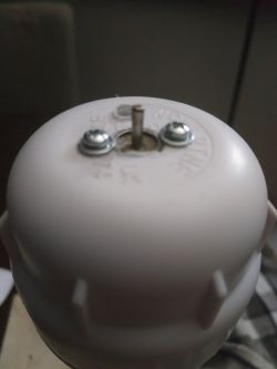 Zbliżenie na pokrywkę plastikową z małą metalową ośką i dwoma śrubami, będącą elementem konstrukcji mini turbiny wiatrowej.