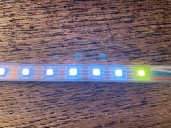 Lit LED strip with white and one yellow LED on a wooden surface