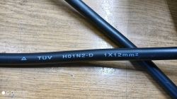 Close-up of H01N2-D Cable Close-up of a black electrical cable with TUV H01N2-D 1X12mm² markings on a wooden surface.