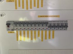 Panel z wyłącznikami elektrycznymi z opisaną listwą na etykietach.