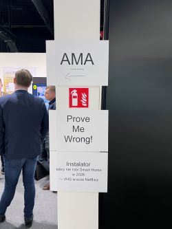 Pillar with “AMA” and “Prove Me Wrong!” signs and a fire extinguisher pictogram at a trade show.