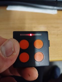 Czarny pilot Nice Ecco5BO z czterema pomarańczowymi przyciskami, na którym świeci się pulsująca czerwona dioda LED.