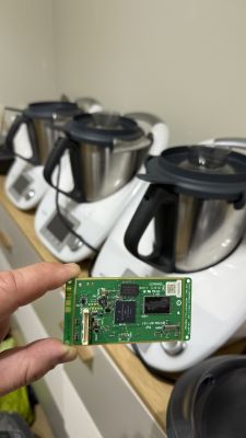 Płyta elektroniczna trzymana przed trzema urządzeniami Thermomix na blacie