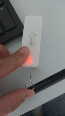 Resetting Temperature and Humidity Sensor Person pressing the reset button on a white temperature and humidity sensor with a red LED light.