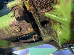Zbliżenie na zabrudzoną i zaolejoną powierzchnię pompy hydraulicznej John Deere z widocznymi śladami wycieku.