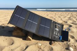 Solar panel on beach angled on wood blocks, connected to device via USB cable