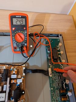 Multimetr pokazujący napięcie 24,9 V na płycie elektronicznej.