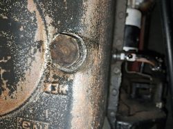 Zbliżenie na rdzewiejącą śrubę w metalowej obudowie, w tle elementy mechaniczne
