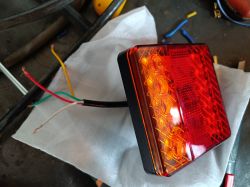 Czerwono-pomarańczowa lampa z wystającymi przewodami leży na białym materiale.