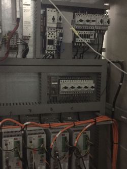 Widok na wnętrze szafy elektrycznej z różnymi komponentami.