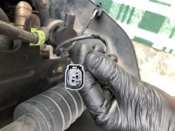 Ręka w rękawiczce trzymająca wtyczkę z dwoma stykami w komorze silnika.